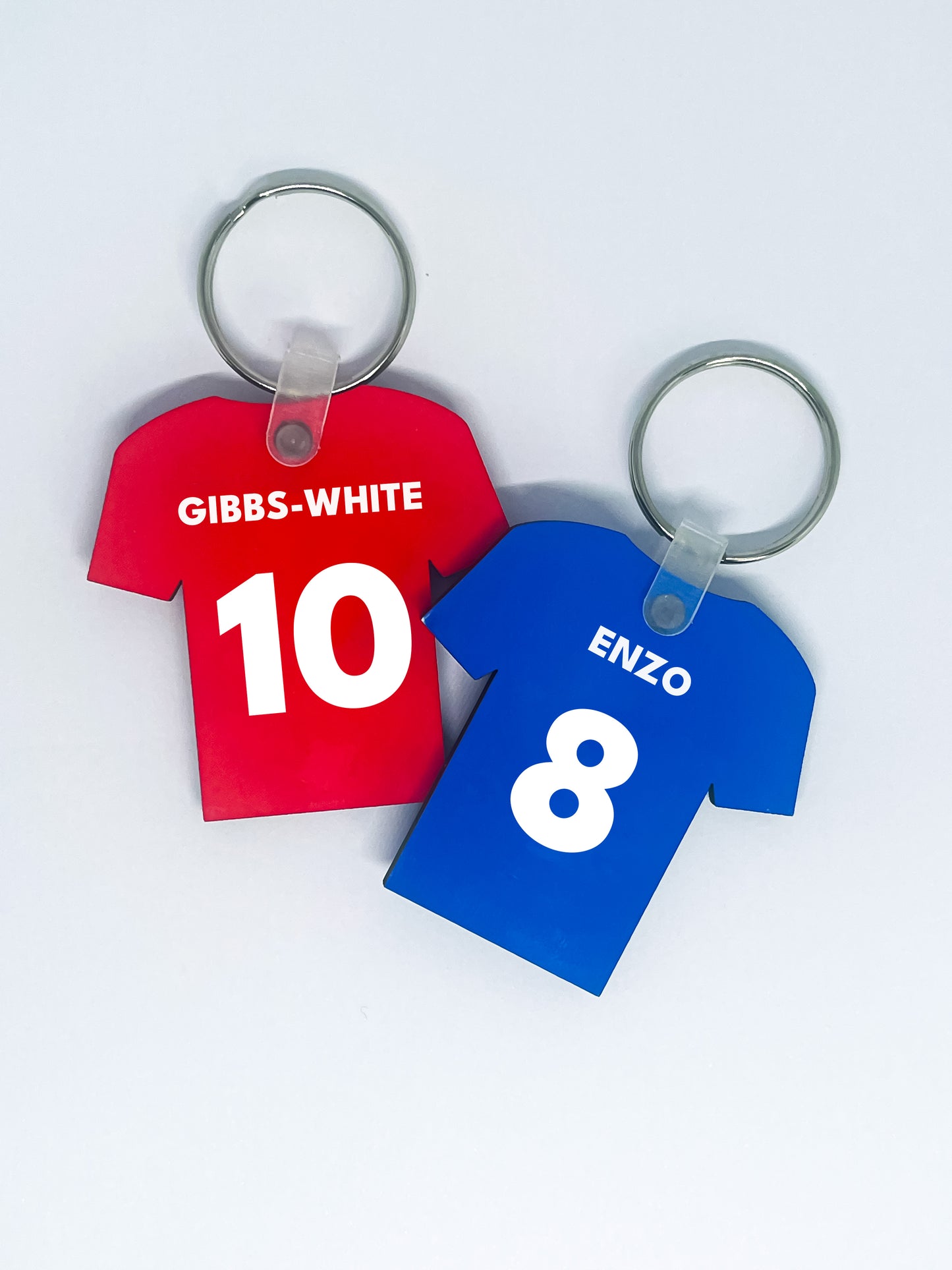 Two keychains shaped like red and blue sports jerseys with names and numbers on a white background.